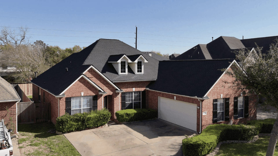 Aerial view of a Houston-area brick home with a new charcoal architectural shingle roof by Rlynt Roofing