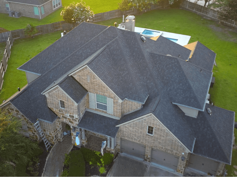 Aerial view of a two-story brick home with a freshly installed charcoal shingle roof by Rlynt Roofing